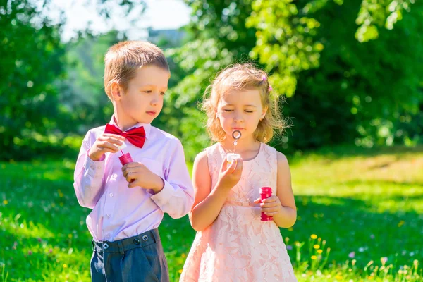 Zes jaar oude jongen kijkt naar het meisje maakt zeepbellen — Stockfoto