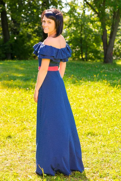 Beautiful brunette woman in a long dress in the park — Stock Photo, Image