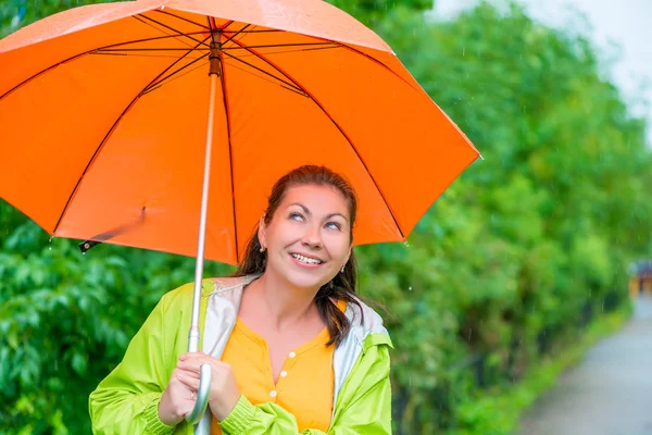 Portrait de brune heureuse portant un imperméable sous un um orange — Photo
