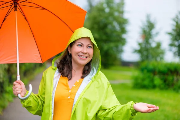 Beautiful girl in a green raincoat and with an umbrella under th — Stock Photo, Image