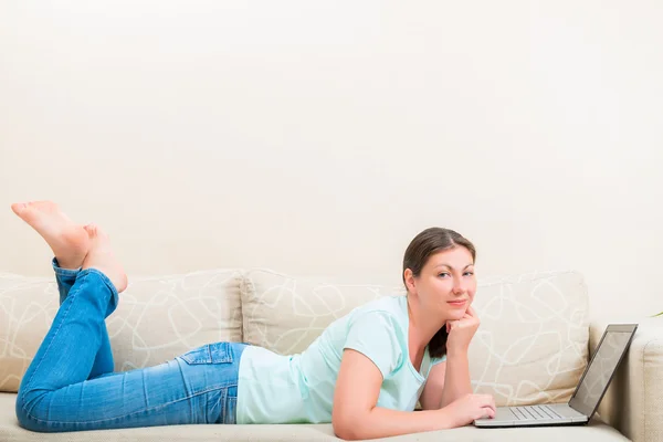 Tjej i jeans och en T-shirt i soffan med en bärbar dator — Stockfoto