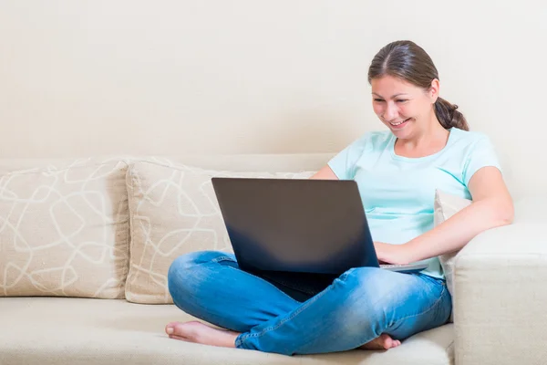 Happy girl communicates online while sitting on a sofa — Stock Photo, Image