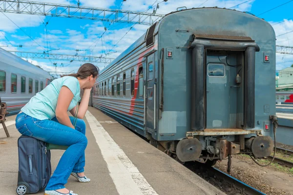 Mulher sentada em uma mala e olhando para o trem de partida — Fotografia de Stock