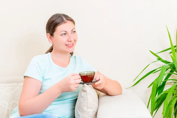 Mooie brunette met een kopje thee op een sofa in de living roo — Stockfoto