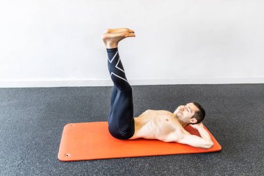 Kafkasyalı genç bir adam paspasın üzerinde hipopresif abdominal egzersizler yapıyor.