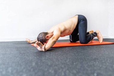 Kafkasyalı genç bir adam paspasın üzerinde hipopresif abdominal egzersizler yapıyor.