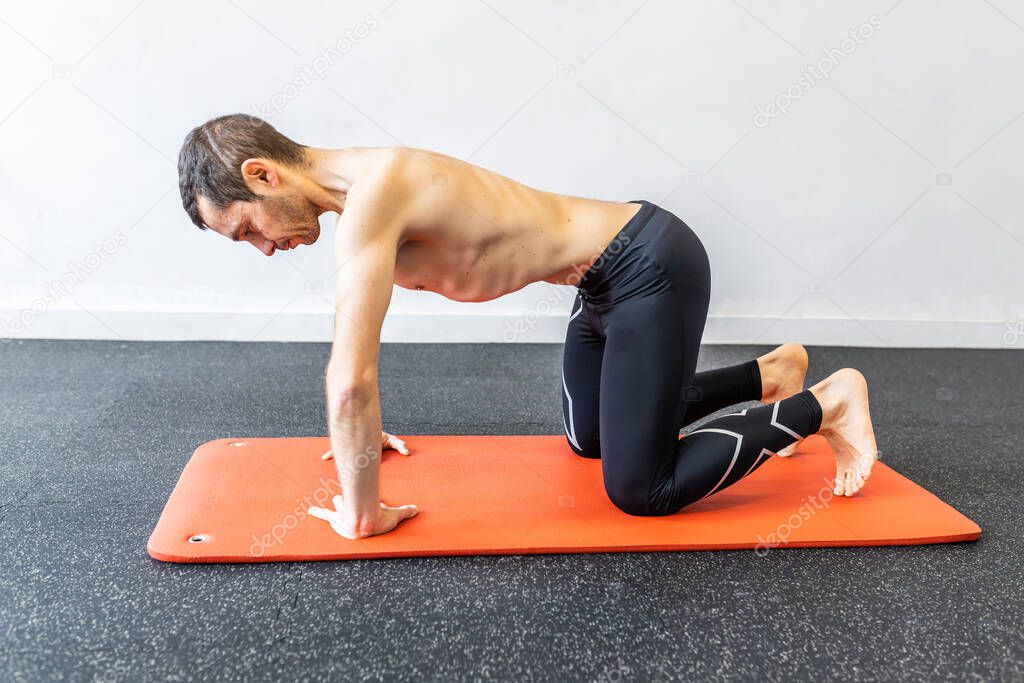 caucasian young adult man training hypopressive abdominal exercises on the mat