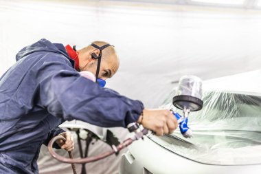 Genç yetişkin erkek araba boyacısı, atölyesinin boya kabinine araba boyuyor.