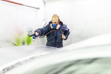 Genç yetişkin erkek araba boyacısı, atölyesinin boya kabinine araba boyuyor.