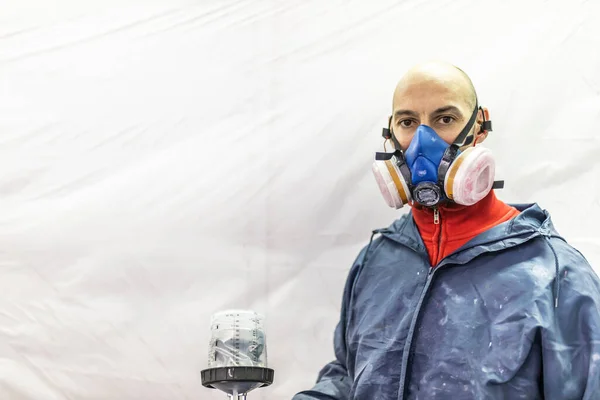 young adult male car painter, painting a car in the paint booth of his workshop