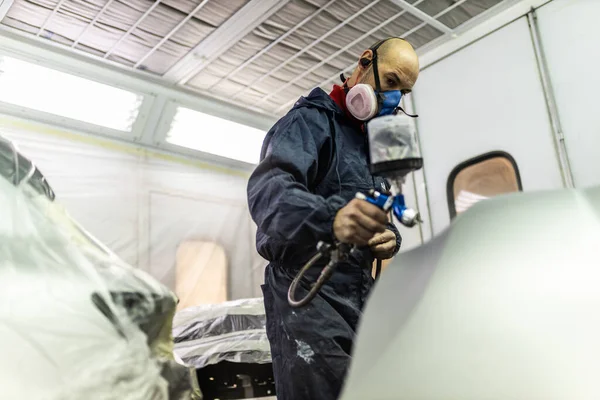 young adult male car painter, painting a car in the paint booth of his workshop