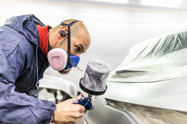 young adult male car painter, painting a car in the paint booth of his workshop