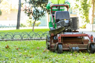 unrecognizable municipal operator mowing the grass with automatic mower in a park