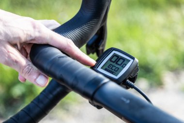 unrecognizable young male cyclist holding his gravel e-bike on a trail, operating the digital control of the electric motor.
