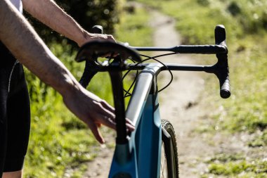 unrecognizable young male bicyclist holding his gravel e-bike on a trail