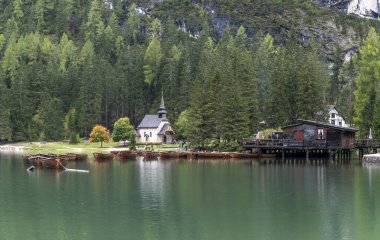 Dolomitlerdeki Pragser Wildsee Gölü. İtalya 'da sonbaharda tekne, dağ, kilise ve orman zinciri..
