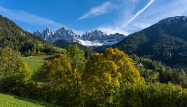Sonbaharda Dolomitler 'deki Geisler Dağları mavi gökyüzü ve sonbahar ağaçlarıyla.