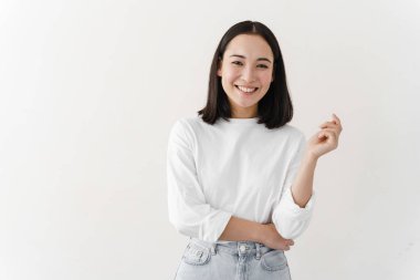 Gülümseyen, güzel esmer beyaz bir duvarda poz veriyor. Genç kadın boş duvarda duruyor..