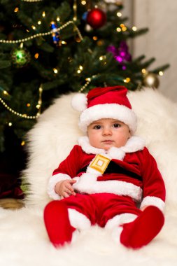 Noel Baba olarak ağacın altında giyinmiş bir çocuk