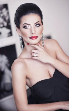 Hairstyle and Make up - beautiful female art portrait with beautiful eyes. Elegance. Genuine natural brunette with black dress without shoulders. Attractive woman with luxurious earrings, indoors shot