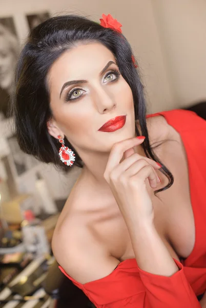 Belle jeune femme avec maquillage créatif et coiffure posant. Brune séduisante à la mode avec un look espagnol, prise de vue intérieure. Portrait de dame en rouge avec fleur dans les cheveux et les yeux magnifiques — Photo