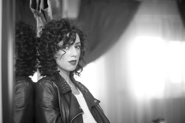 Charming young curly brunette woman with black leather jacket. Sexy gorgeous young woman with modern look. Portrait of sensual girl with voluptuous mouth feeling sad, black and white indoors shot — Zdjęcie stockowe