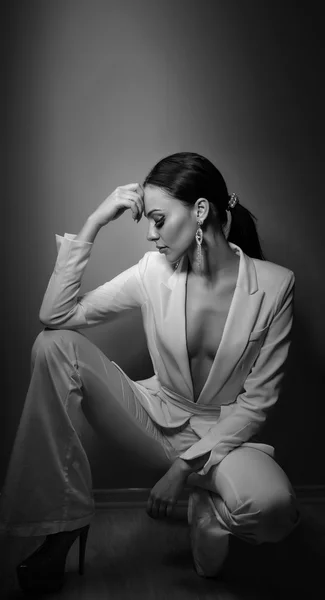 Young beautiful brunette woman in elegant white suit with trousers sitting. Seductive dark hair girl posing, studio shot. Elegant lady in white suit with jacket with plunging neckline, nostalgia — Stock Photo, Image