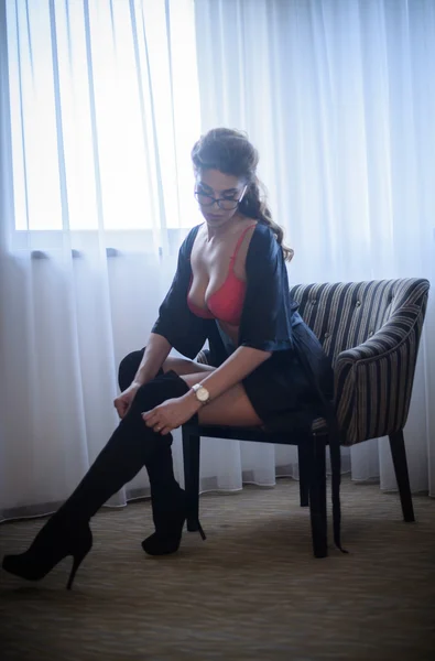 Attraktive Frau in roten Dessous posiert auf einem Sessel sitzend mit weißen Vorhängen im Hintergrund. Porträt eines sinnlichen Mädchens mit perfekten Beinen und langen schwarzen Strümpfen. sexy Frau mit langen lockigen Haaren drinnen — Stockfoto