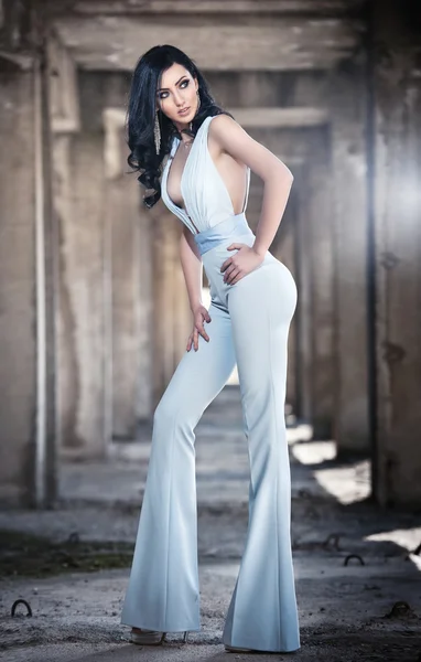 Portrait of beautiful sexy young woman with elegant overall, in urban background. Attractive young brunette with long hair and blue eyes posing fashion in white outfit. Long legs woman, side view — Stock Photo, Image