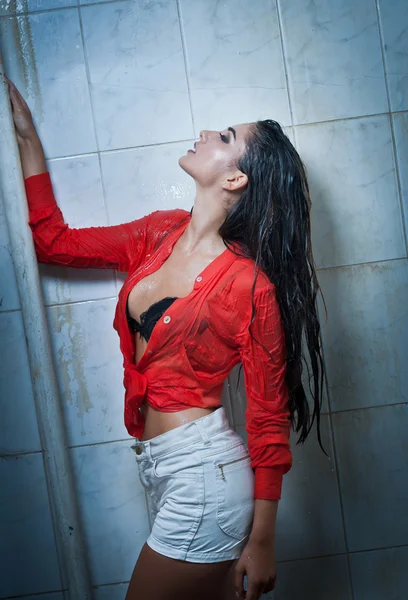 完璧なボディの濡れた髪と透明な赤いシャツ 完璧なぽっちゃりボディのシャワーの下で官能的なポーズでポーズをとるかわいいブルネットの女性 濡れたシャツでうれしそうな少女の肖像画 — ストック写真
