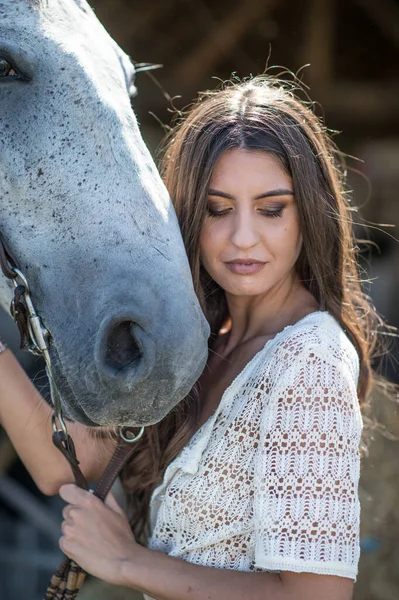 長い髪 長い白いドレスと馬と美しいブルネットの女性 少女と馬の肖像画 官能的で魅力的な女の子が交流し 牧場で馬と楽しんでいます — ストック写真