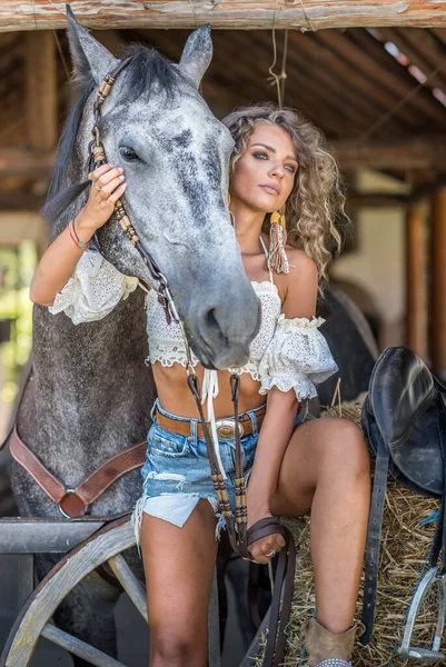 巻き毛と馬を持つ美しいブロンドの女性 デニムと馬を持つ少女の肖像画 美しい女の子が交流し 牧場で馬と楽しい時間を過ごしています — ストック写真