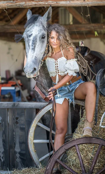 美丽的金发女人 卷曲的头发和马 一个穿着斜纹棉布和马的女孩的画像 美丽的女孩在农场里和一匹马交流和玩乐 — 图库照片