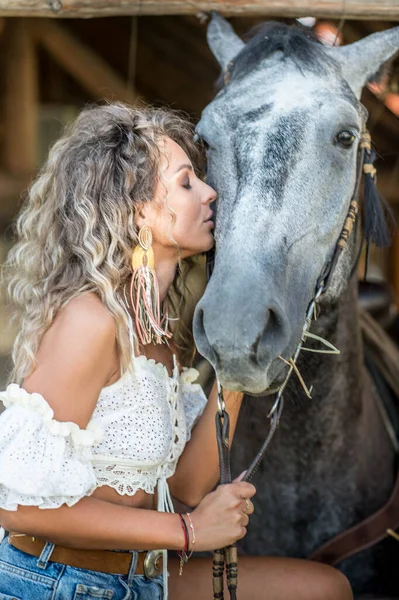 巻き毛と馬を持つ美しいブロンドの女性 デニムと馬を持つ少女の肖像画 美しい女の子が交流し 牧場で馬と楽しい時間を過ごしています — ストック写真