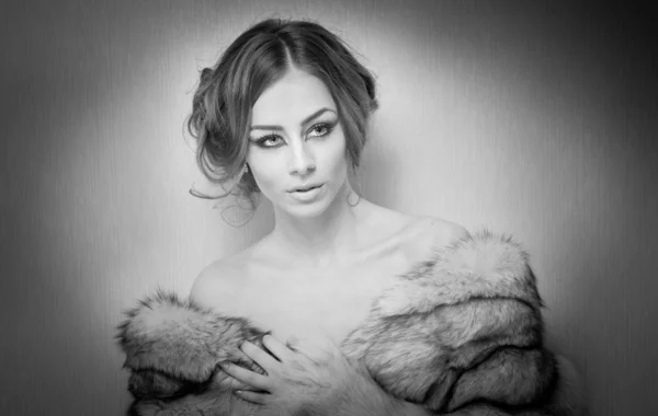 Attractive sexy young woman wearing a fur coat posing provocatively indoor. Black and white portrait of sensual female with creative haircut, studio shot. Beautiful girl covered only with a fur — Stock Photo, Image