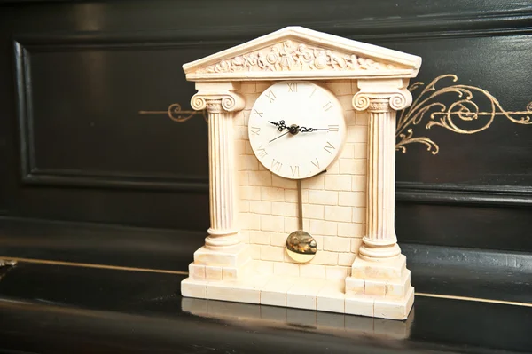 Jam antik yang elegan. Jam dengan kuil Yunani. Jam marmer pada piano hitam — Stok Foto