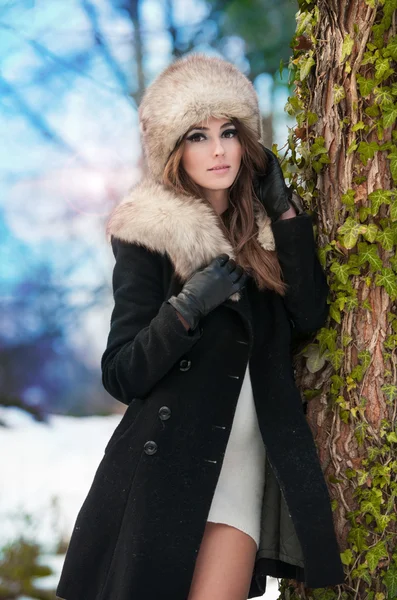 Retrato de jovem mulher bonita, tiro ao ar livre em cenário de inverno. Menina morena sensual com casaco e boné de pele posando em um parque coberto de neve. Mulher na moda em um dia frio . — Fotografia de Stock