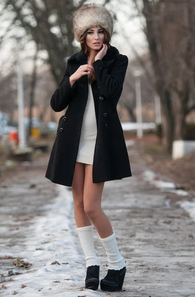 Портрет молодой красивой женщины, съемка на открытом воздухе в зимнем пейзаже. Чувственная брюнетка в пальто и меховой шапке позирует в парке, покрытом снегом. Модная женщина в холодный день . — стоковое фото