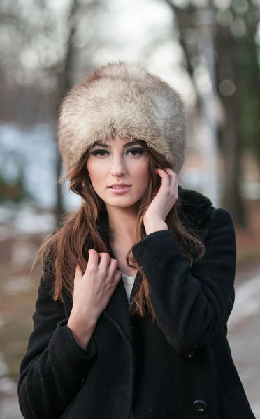 Ritratto di giovane bella donna, ripresa all'aperto nel paesaggio invernale. Sensuale ragazza bruna con cappotto e berretto di pelliccia in posa in un parco coperto di neve. Donna alla moda in un giorno freddo . — Foto Stock