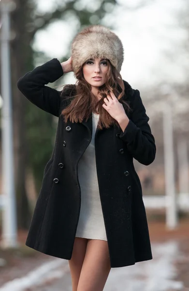 Retrato de mujer hermosa joven, tiro al aire libre en el paisaje de invierno. Chica morena sensual con abrigo y gorra de piel posando en un parque cubierto de nieve. La hembra a la moda en el día frío . —  Fotos de Stock