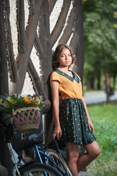 Belle fille portant une belle robe avec look collège s'amusant dans le parc avec vélo portant un beau panier. Paysages anciens. Jolie fille blonde rétro avec vélo et panier avec des fleurs — Photo