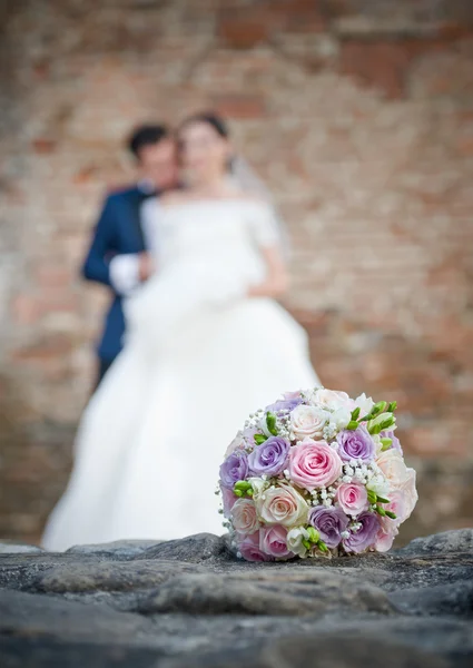 Newly-married couple and wedding bouquet in the foreground. Wedding bouquet with the wedding couple in the background — Stock Photo, Image