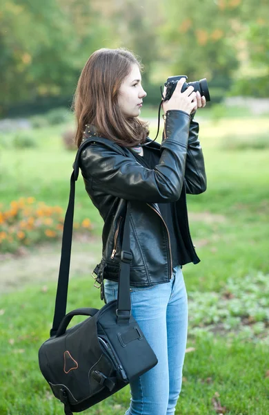 Atrakcyjny dziewczynka fotografowanie na zewnątrz. Cute nastolatka w niebieskie jeansy i czarną skórzaną kurtkę robienia zdjęć w jesienny park. Zewnątrz portret ładna nastolatka zabawy w parku z aparatu — Zdjęcie stockowe