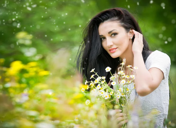 Beautiful young woman in wild flowers field.Portrait of attractive brunette girl with long hair relaxing in nature, outdoor shot in sunny day. Lady in white enjoying daisy field, harmony concept — Stock Photo, Image