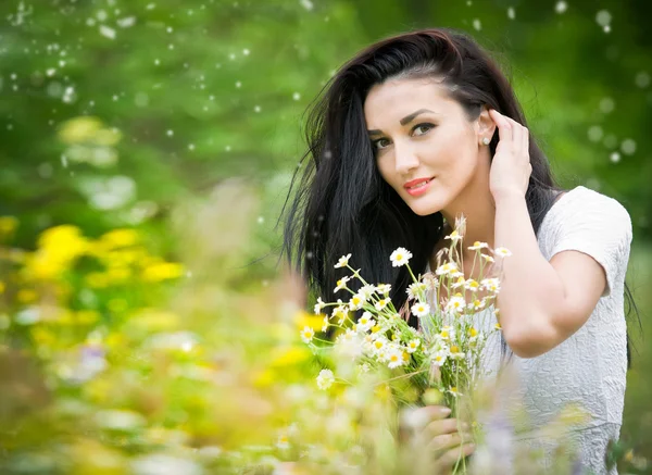 Hermosa mujer joven en el campo de flores silvestres.Retrato de chica morena atractiva con el pelo largo relajante en la naturaleza, tiro al aire libre en el día soleado. Dama de blanco disfrutando del campo de margaritas, concepto de armonía —  Fotos de Stock