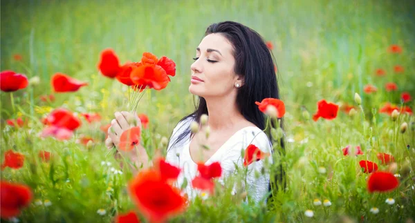 Jovem relaxante no campo de papoilas verdes. Retrato de bela mulher morena posando em um campo cheio de papoilas. Mulher bonita apreciando as flores selvagens vermelhas brilhantes, conceito de harmonia — Fotografia de Stock