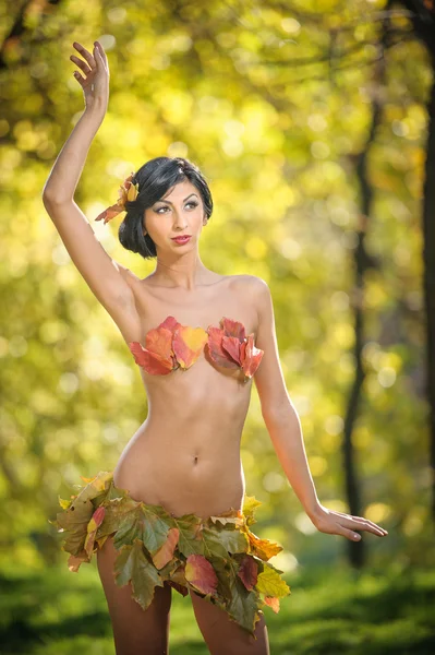 Photo of sensual brunette girl posing in a beautiful autumnal park dressed with a suit made by rusty leaves. Elegant female covered by autumn leaves. Young woman enjoying autumnal sunny day in park — Stock Photo, Image