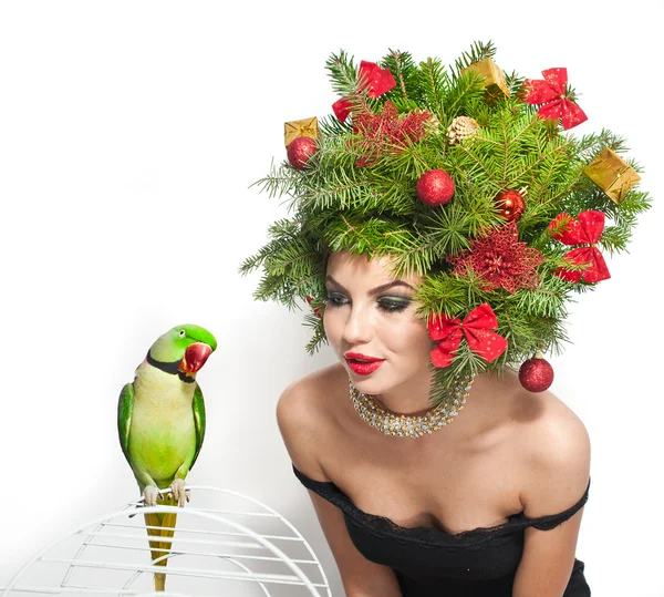 Hermoso maquillaje creativo de Navidad y estilo de pelo tiro interior. Chica modelo de moda de belleza. El invierno. Hermosa chica atractiva con accesorios de árbol de Navidad en el estudio hablando con un loro verde . — Foto de Stock