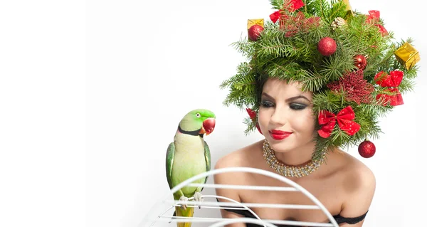 Hermoso maquillaje creativo de Navidad y el estilo de pelo de la sesión de interior. Chica modelo de moda de belleza. El invierno. Hermosa chica con loro verde en el estudio. Chica atractiva con accesorios de árbol de Navidad —  Fotos de Stock