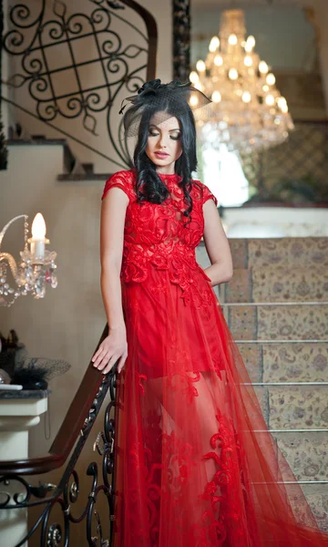 La bella ragazza in un abito lungo rosso in posa in una scena vintage. Giovane bella donna che indossa un vestito rosso in un vecchio hotel. Sensuale elegante giovane donna in abito rosso lungo indoor shot . — Foto Stock